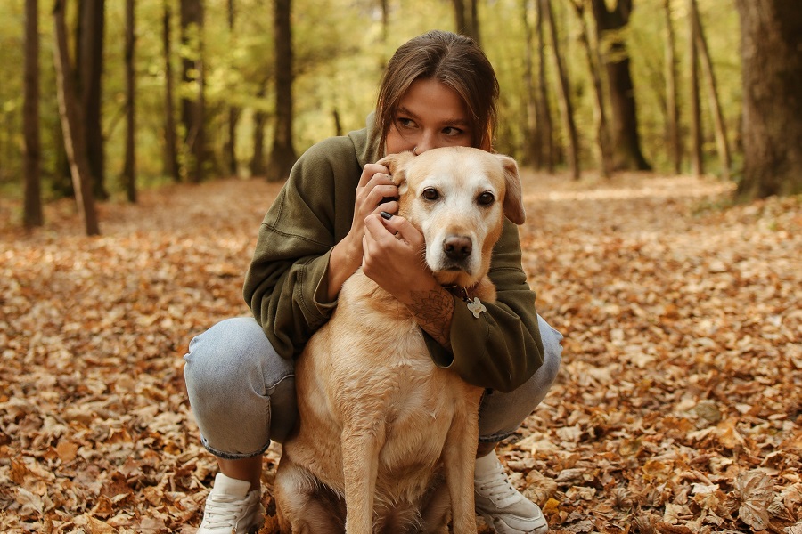 Fall Nail Designs a Woman Kneeling Down Hugging Her Dog on a Hiking Trail During Fall