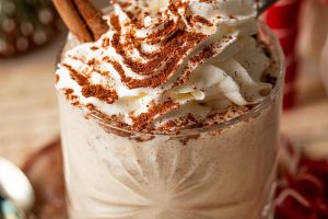 Bourbon Eggnog Recipe Close Up of a Glass of Eggnog Topped with Whipped Cream and Cinnamon with a Cinnamon Stick Sticking Out of the Cream