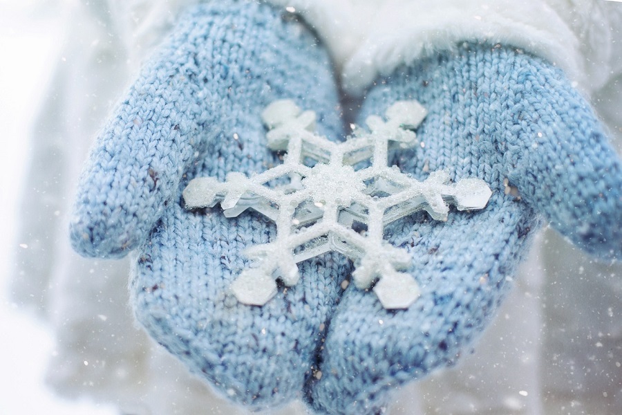 DIY Christmas Decor Ideas Close Up of a Person's Hands in Blue Knit Mittens Holding a Fake Snowflake