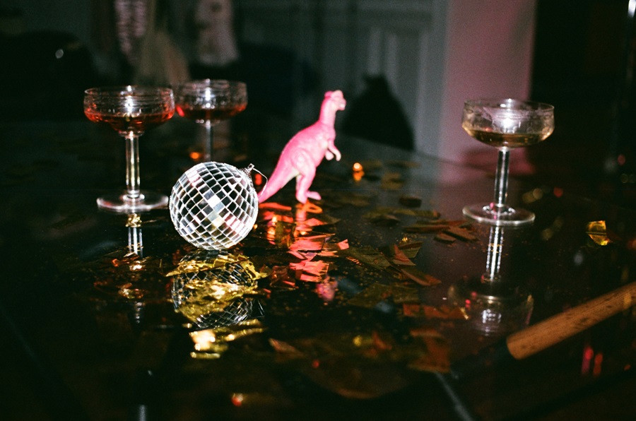 New Years Eve Outfits a Disco Ball and a Pink T-Rex Toy on a Table with Cocktails Around Them