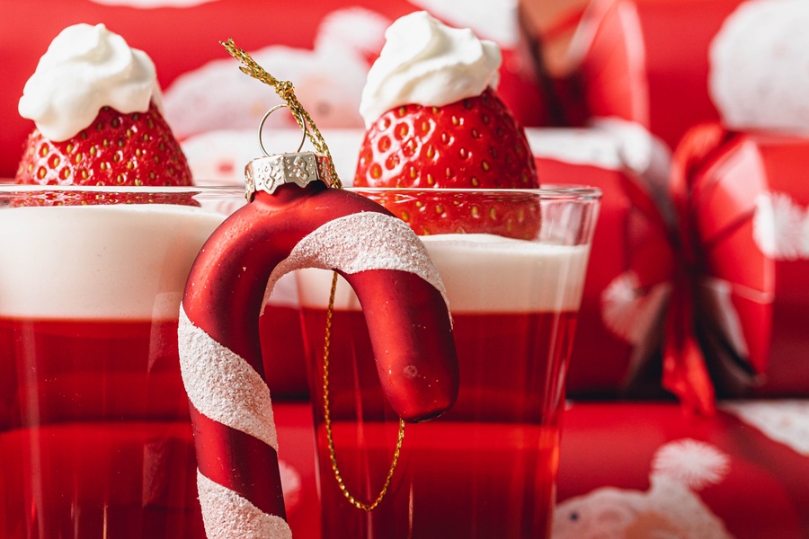 Easy Santa Hat Jello Shot Recipe Close Up of a Candy Cane Leaning Against Jello Shots in Glasses