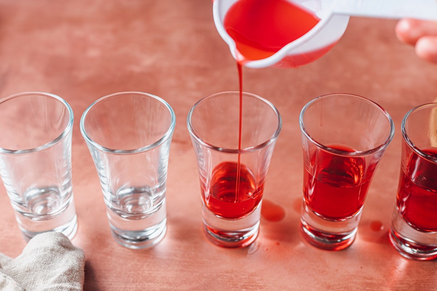 Easy Santa Hat Jello Shot Recipe Close Up of Jello Mixture Being Poured into Small Shot Glasses