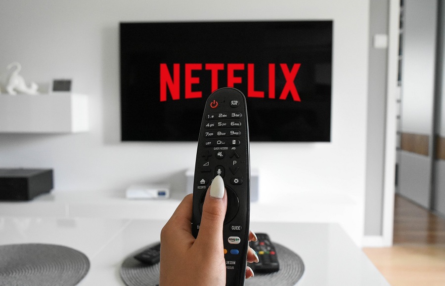 Netflix Shows You May Have Missed Close Up of a Remote Held Up with a TV in the Background That Says Netflix