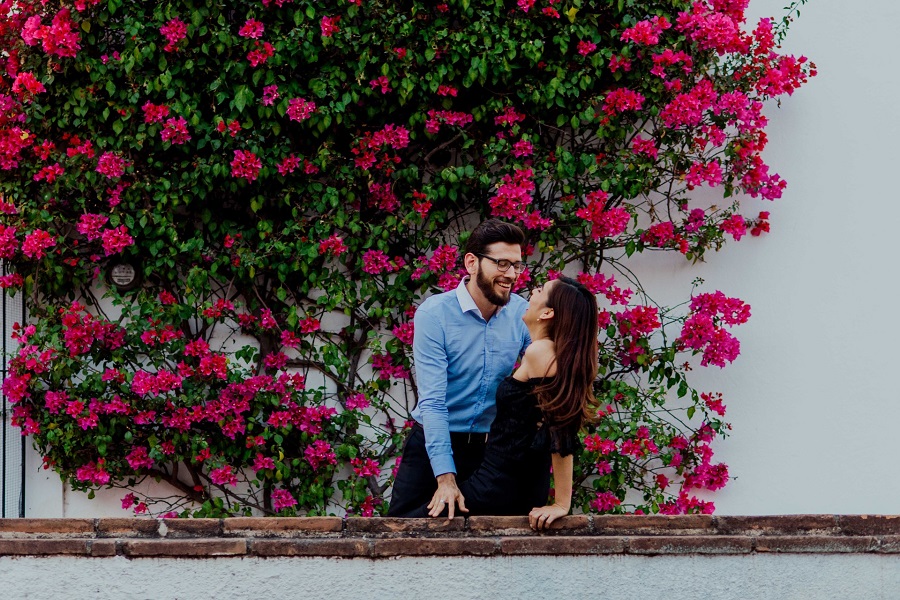 Sarcastic Valentines Day Quotes for Couples a Couple Laughing Together with a Wall Covered in Flowers Behind Them