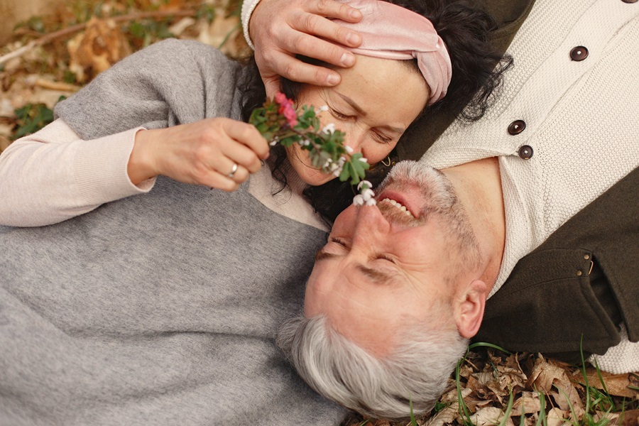Valentines Photoshoot Ideas an Older Couple Laying on the Ground Looking at Flowers and Smiling