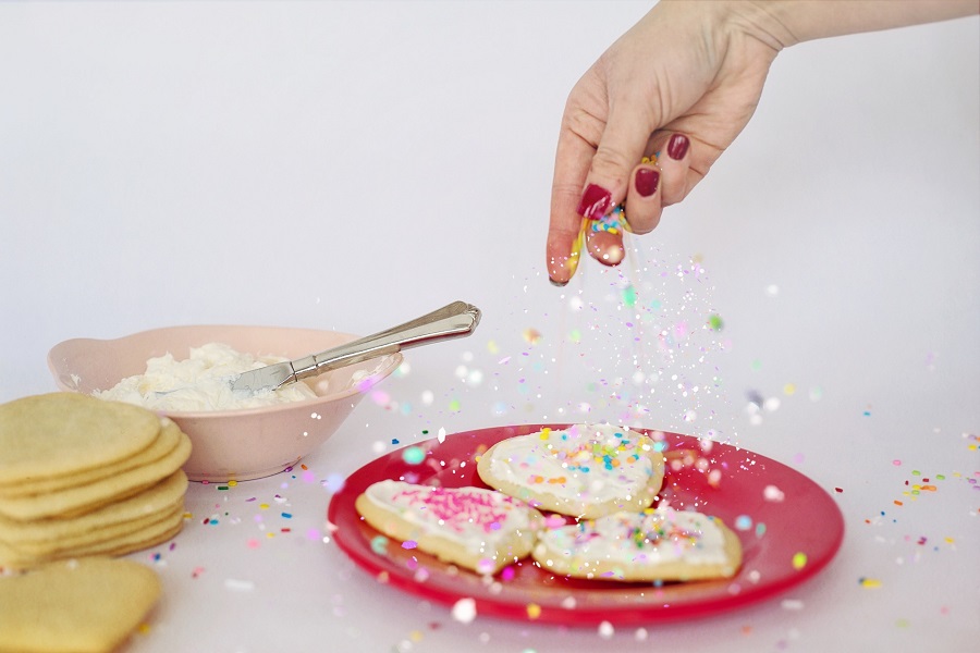 Valentines Cookies Close Up of a Woman's Hand Sprinkling Sprinkles Over Heart-Shaped Cookies on a Red Plate