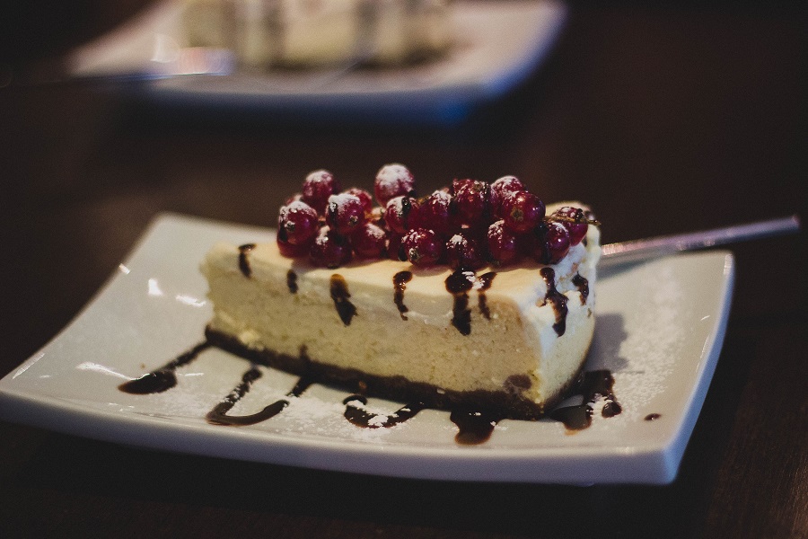 Valentines Day Desserts for Two Close Up of a Slice of Cheesecake Topped with Fruit and Drizzled with Chocolate Syrup