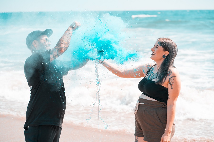Cool Gender Reveal Ideas for Spring Man and Woman Standing on a Beach Doing a Powder Gender Reveal with Blue Powder