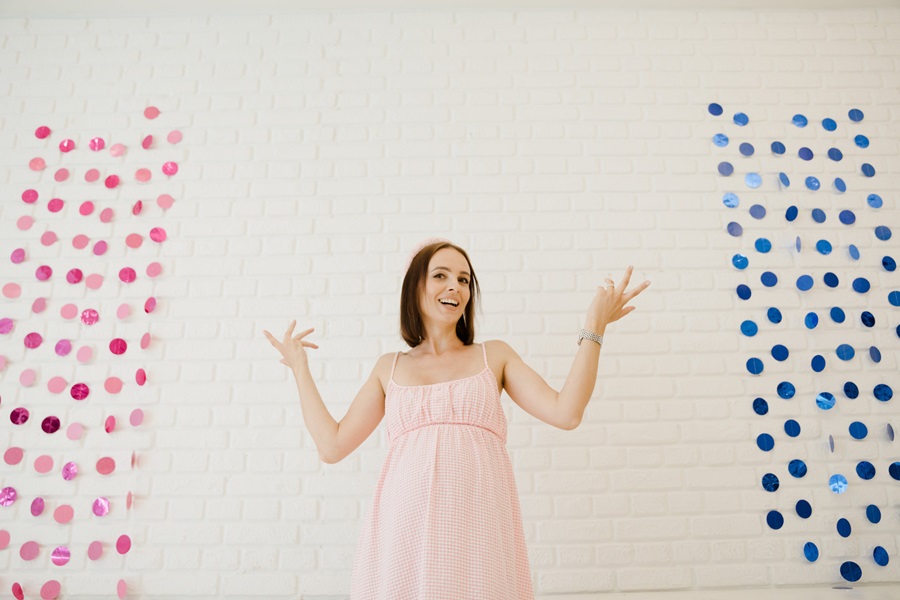 Gender Reveal Ideas for Spring a Woman Standing with Her Hands Pointing To Either Side with a Pink Banner on One Side and a Blue Banner on the Other