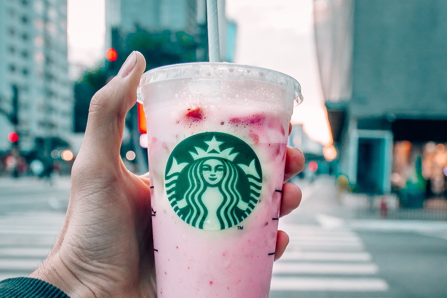 Starbucks Secret Menu Refreshers Drink Recipes Close Up of a a Person Holding Up a Pink Drink in a Starbucks Cup with a City in the Background