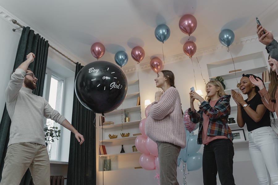 Cool Gender Reveal Ideas for Spring People Standing Around in a Living Room About to Pop a Black Balloon That Says He or She
