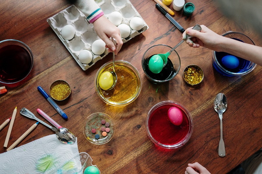 Easter Quotes to Share This Spring Overhead View of a Kitchen Table with Kids Dying Eggs for Easter in Different Colors Including Red, Green, and Yellow