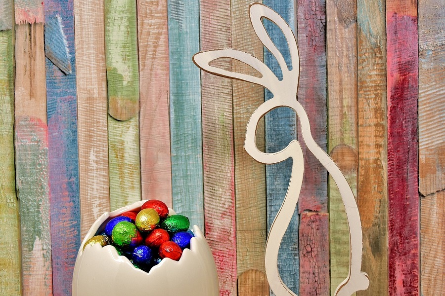 Easter Decorations for Parties Close Up of a Wooden Bunny Outline Standing Next to a Cracked Open Egg Filled with Chocolates