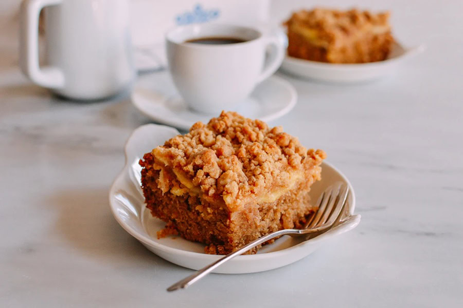 Brunch Recipes for Mother's Day Apple Cinnamon Coffee Cake on a Plate with a Fork and a Cup of Coffee in the Background