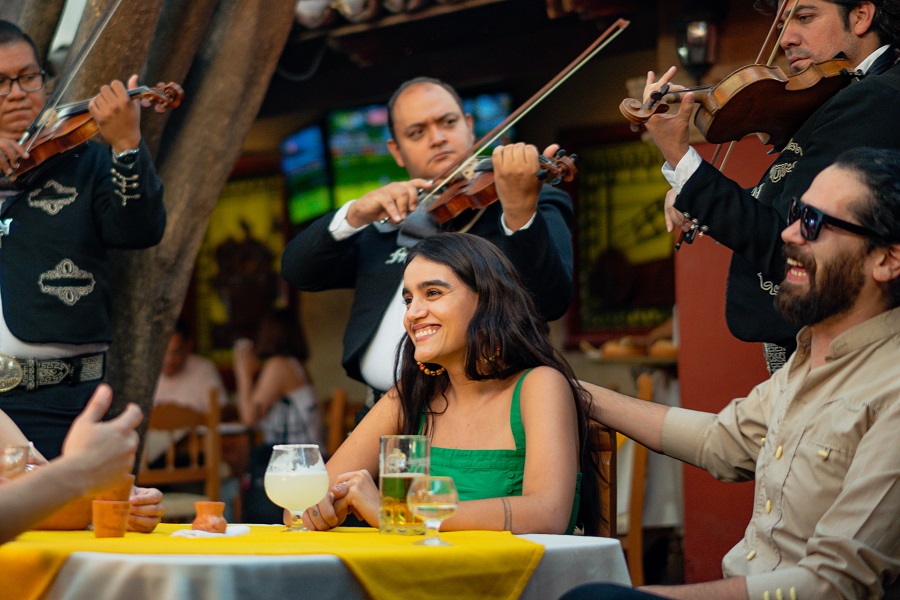 Cinco de Mayo Quotes Woman Sitting at a Table Outside with a Mariachi Band Playing Music Behind Her