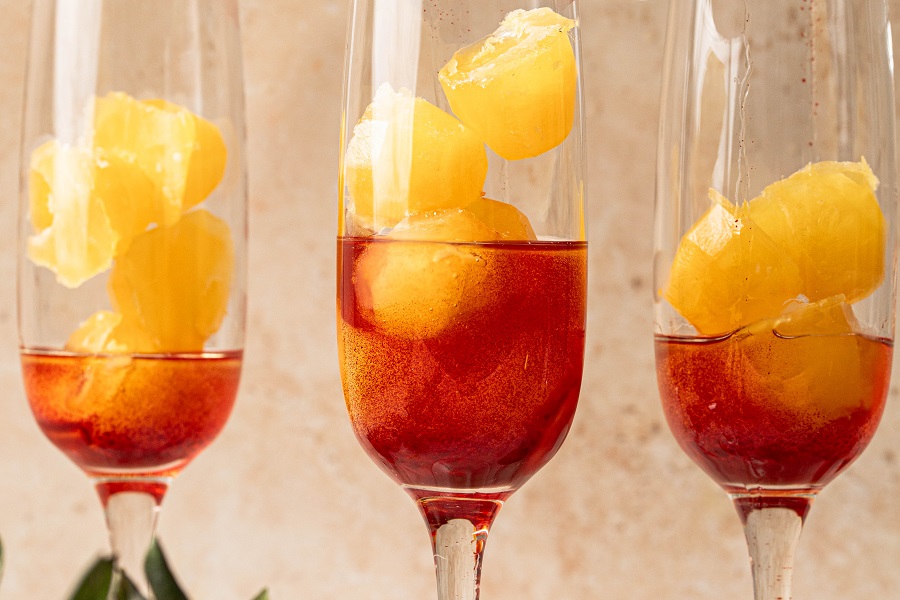 Sunrise Strawberry Mimosa Recipe Close Up of a Champagne Flute with Strawberry Simple Syrup and Orange Juice Ice Cubes