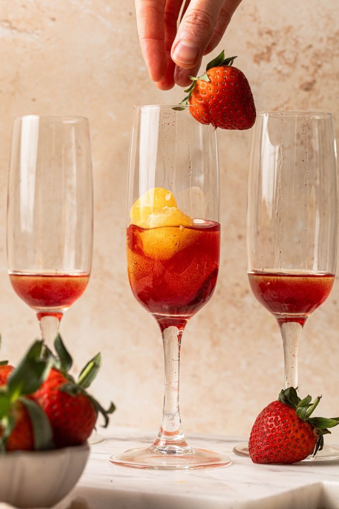 Sunrise Strawberry Mimosa Recipe Close Up of a Champagne Flute with Strawberry Simple Syrup and Orange Juice Ice Cubes