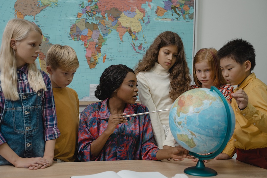 Best Teacher Appreciation Gift Ideas a Teacher Pointing to a Globe with Students Surrounding Her