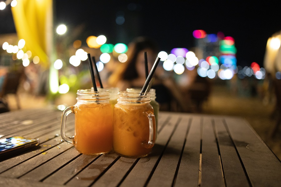 DIY Outdoor Lighting Close Up of Two Cocktails Sitting on a Table Outside with a Party Going on in the Background at Night