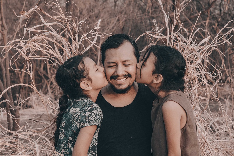 Funny Fathers Day Quotes a Father Sitting in Some Tall Grass Being Kissed on His Cheeks By His Two Daughters