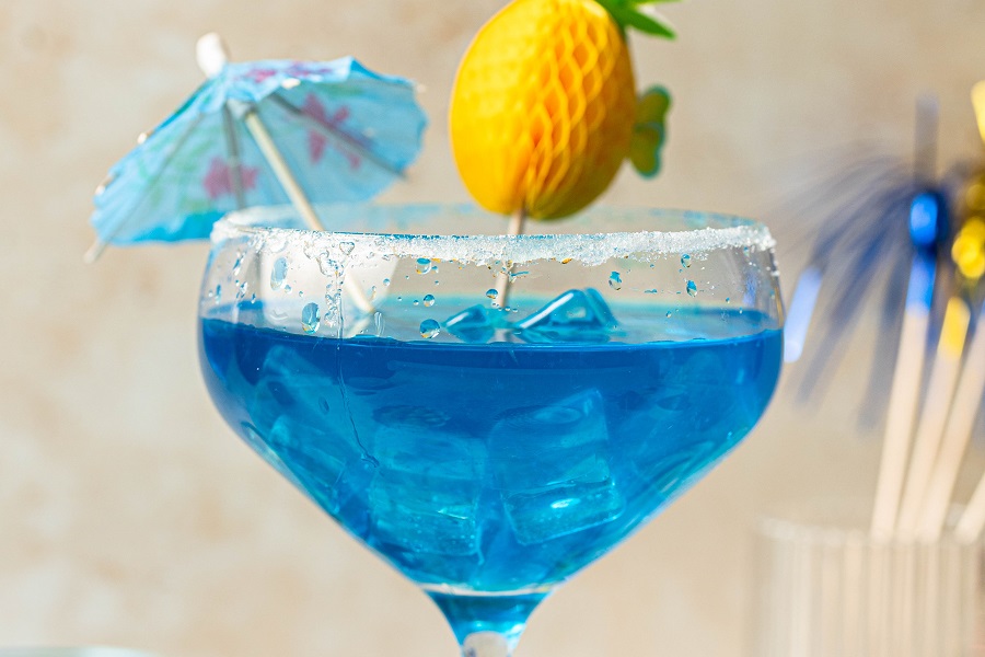 Large Batch Cocktails Close Up of a Blue Margarita Garnished with a Small Paper Pineapple and an Umbrella