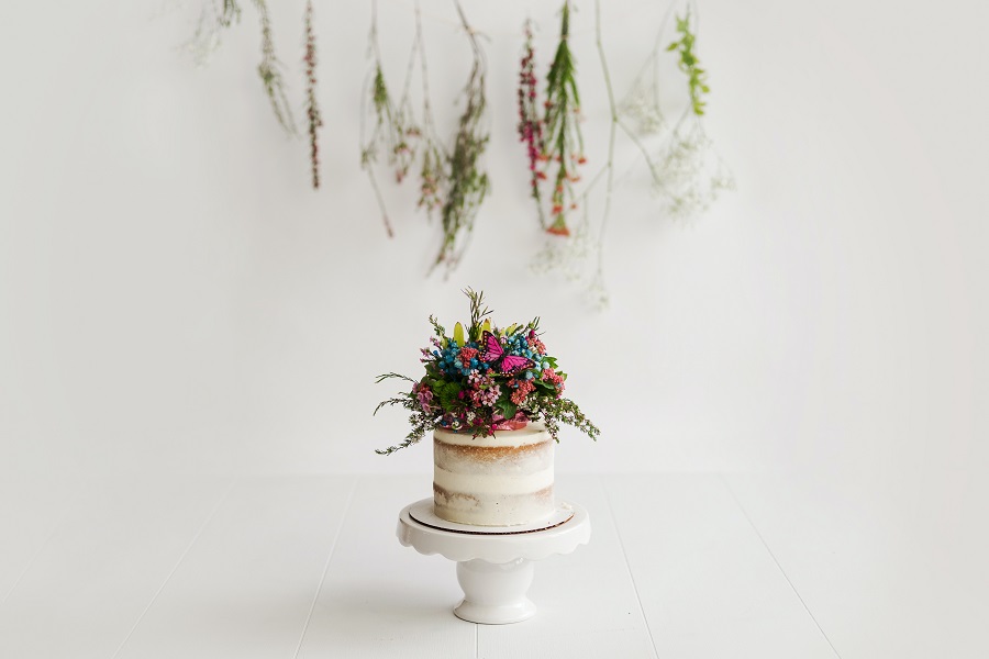 Naked Cake Decorating Ideas View of a Naked Cake Sitting on a Cake Platter with Flowers on Top and Plants Hanging in the Background
