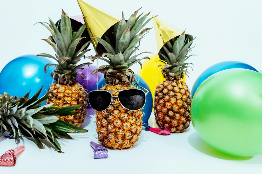 Easy Summer Dinner Party Tips Three Pineapples One with Sunglasses On Next to Colorful Balloons on a White Background
