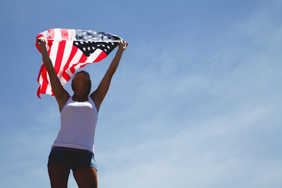 4th of July Nail Designs a Woman Standing Outside with Her Hands in the Air Holding an American Flag That is Waving in the Wind Backward