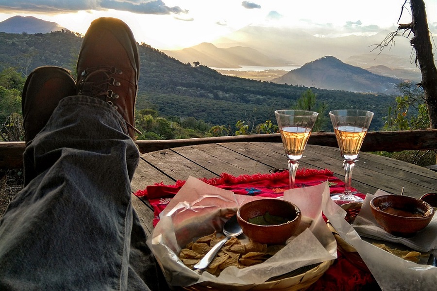 Summer Dinner Party Tips View of a Man Sitting at a Table with His Feet Up and Two Glasses of Wine Next to some Plates of Food