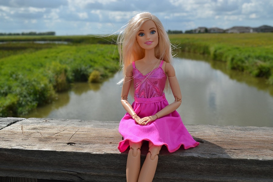 Barbie Movie Quotes a Barbie Doll Sitting on the Railing of a Bridge Above a Small Creek