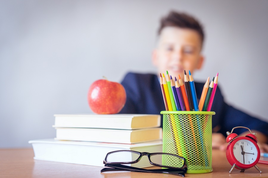 Best Back to School Party Ideas Close Up of a Pencil Tin, a Stack of Books and an Apple with a Student in the Background