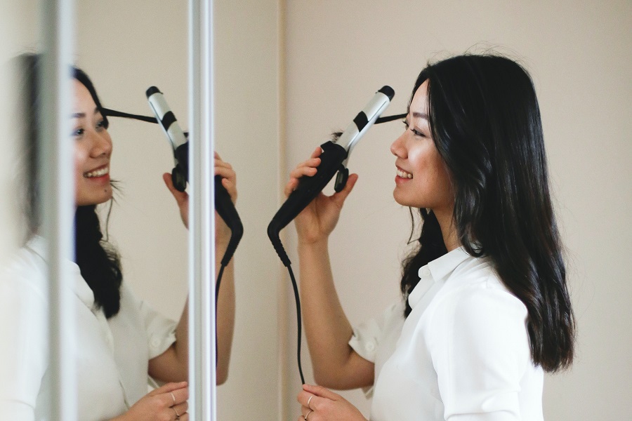 Easy Back to School Hairstyles a Woman Doing Her Hair in the Mirror with a Curling Iron
