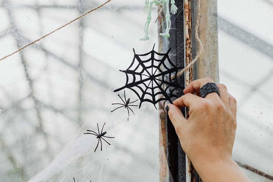 Indoor Halloween Decor Ideas Close Up of a Hand Placing a Fake Black Spider Web On a Window