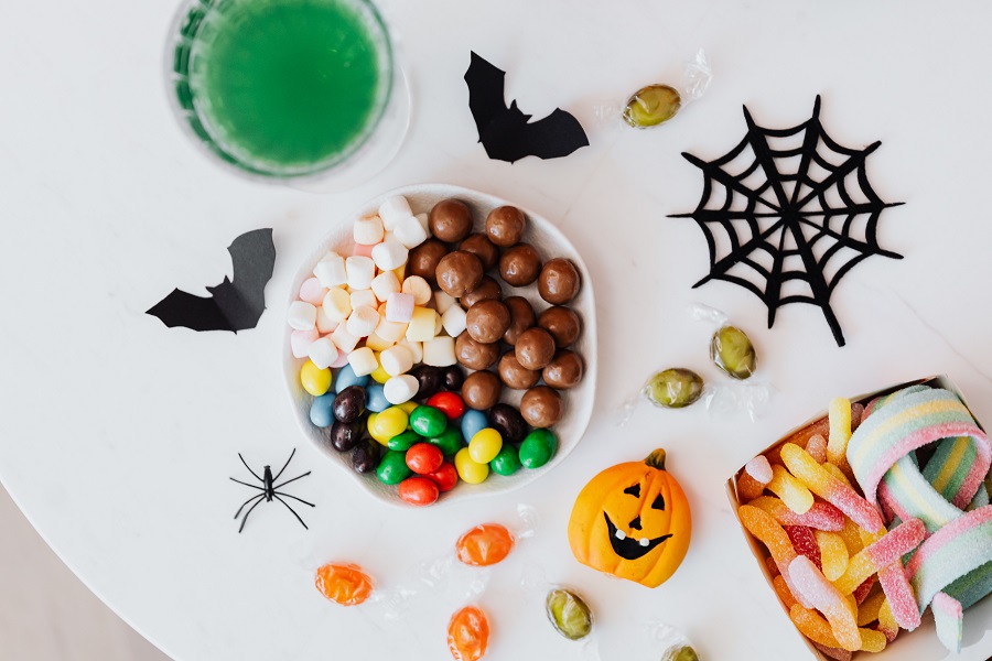 Candy Cocktail Recipes for Halloween Overhead View of a Small Bowl Filled with Chocolates Surrounded By Halloween Toys