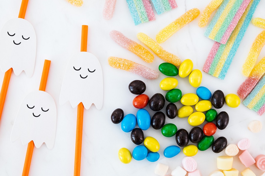 Candy Cocktail Recipes for Halloween Three Small Ghost Toys Next to Colorful Candies on a White Surface