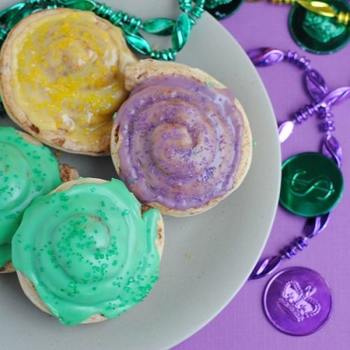 Easy Mini King Cake Recipe Close Up of Finished Mini King Cakes on a Plate Next to Mardi Gras Beads and Tokens