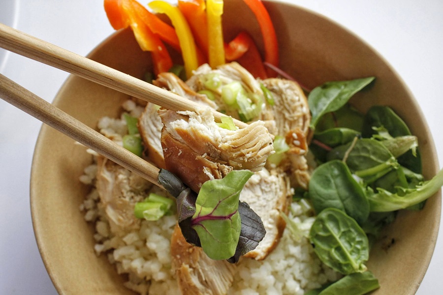 Healthy Teriyaki Chicken Recipe Close Up of Teriyaki Chicken In-between Chopsticks Above a Bowl of Brown Rice
