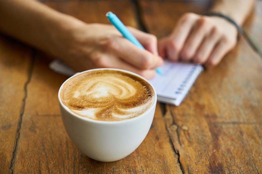 Best Coffee Wine Bar Ideas a Person Writing in a Small Notepad Next to a Cup of Coffee on a Wooden Table