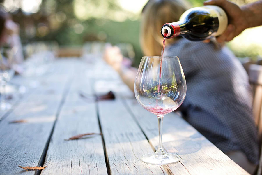 Casual Dinner Party Menu Ideas Close Up of a Person Pouring Red Wine into a Glass on a Wooden Table Outdoors