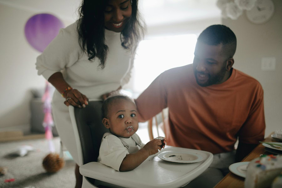 1st Birthday Party Ideas for Boys a Mom and Dad Looking at Their Baby Boy Sitting in a High Chair Eating Cake 