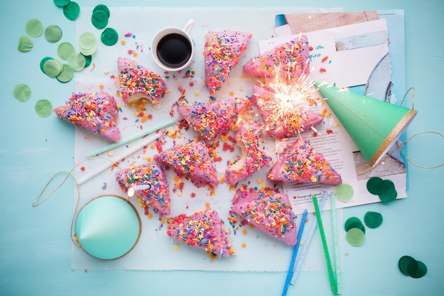 1st Birthday Party Ideas for Girls Close Up of Pink Scones on a Light Blue Table with Party Hats and Confetti