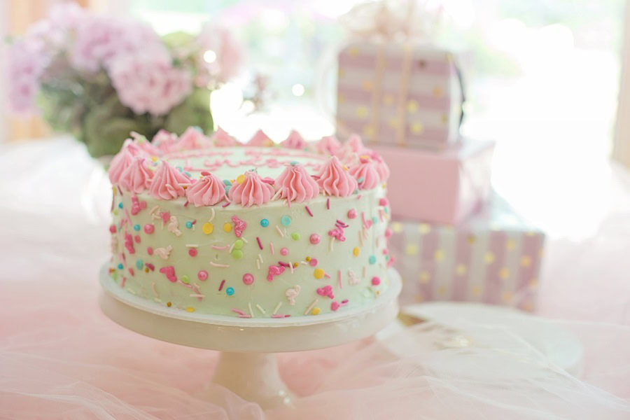 1st Birthday Party Ideas for Girls Close Up of a White and Pink Cake on a Table with Gifts Wrapped in Pink Paper in the Background