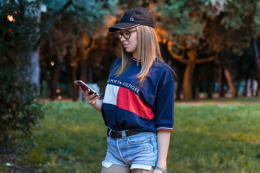 Women's Jort Outfit Ideas a Woman Wearing a Baggy Tommy Hilfiger Shirt and Jorts Standing Outside in a Park