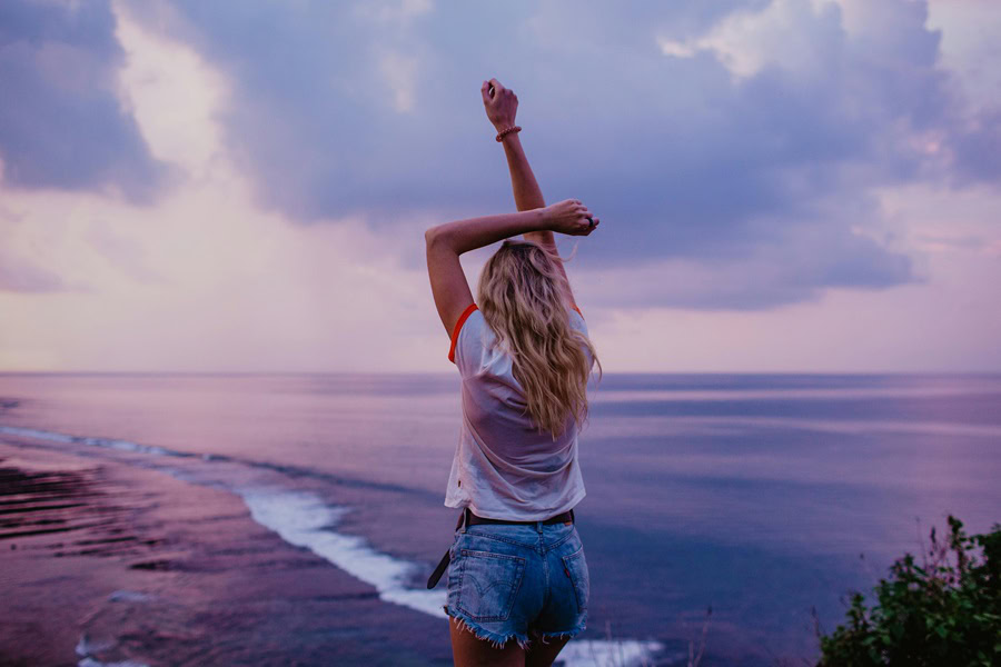 Women's Jort Outfit Ideas a Woman in a Baby Tee and Jorts Standing on a Cliff Above an Ocean