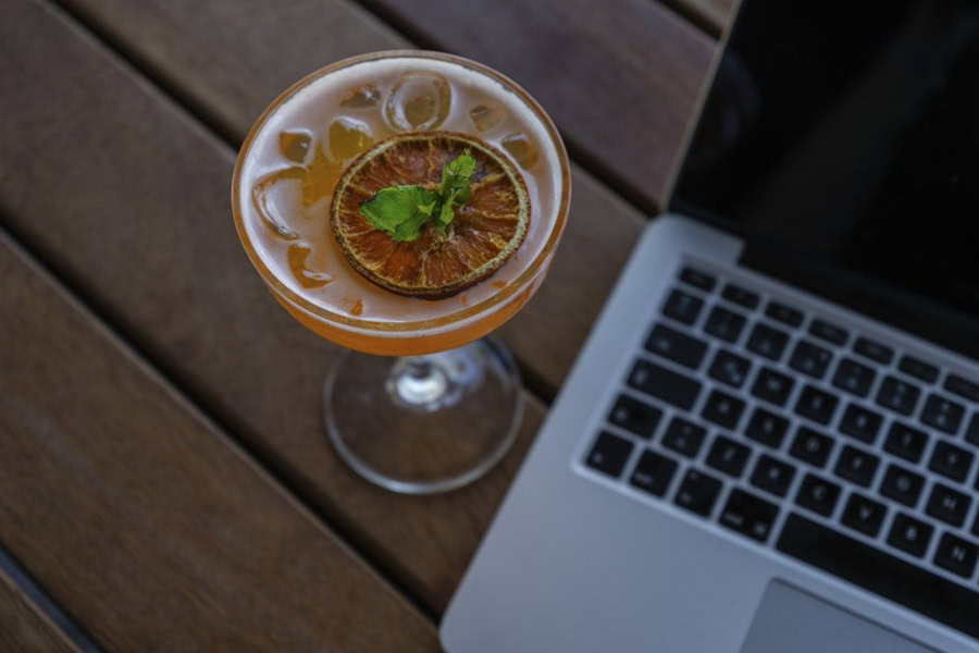 Big Batch Cocktails for Fall a Cocktail with a Blood Orange Slice on a Table Next to a Laptop