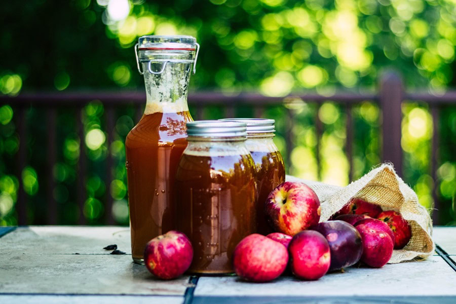 Big Batch Cocktails for Fall a Pitcher and Two Mason Jars Filled with Apple Cider on a Table with Red Apples