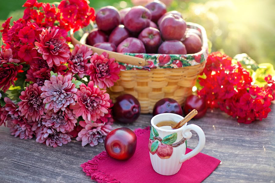 Big Batch Cocktails for Fall a Cup with Liquid Inside Next to a Basket of Red Apples and Red Flowers