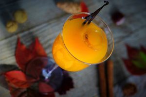 Big Batch Cocktails for Fall Close Up of an Orange Cocktail Surrounded with Fall Leaves