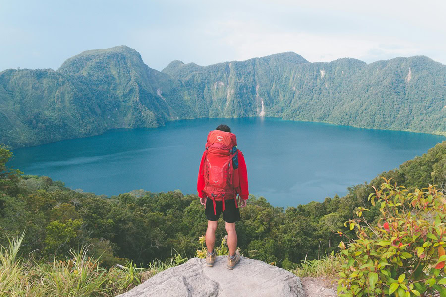 Funny Backpacking Quotes A Person Standing at The Edge of Wearing a Red Hiking Backpack Overlooking a Lake Surrounded by Mountains