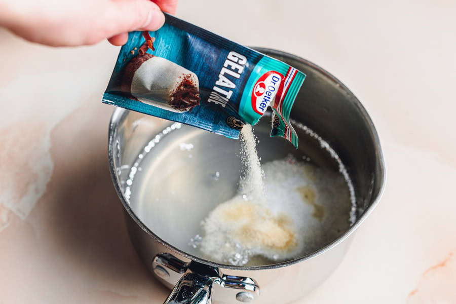 Champagne Jello Shots Recipe a Person's Hand Pouring Gelatin Powder into a Silver Pot